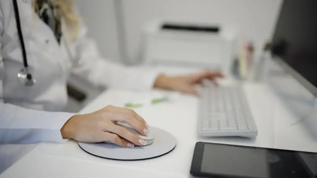 AI is changing everyday work: Doctor working at a desk using a computer mouse and keyboard in a medical office setting